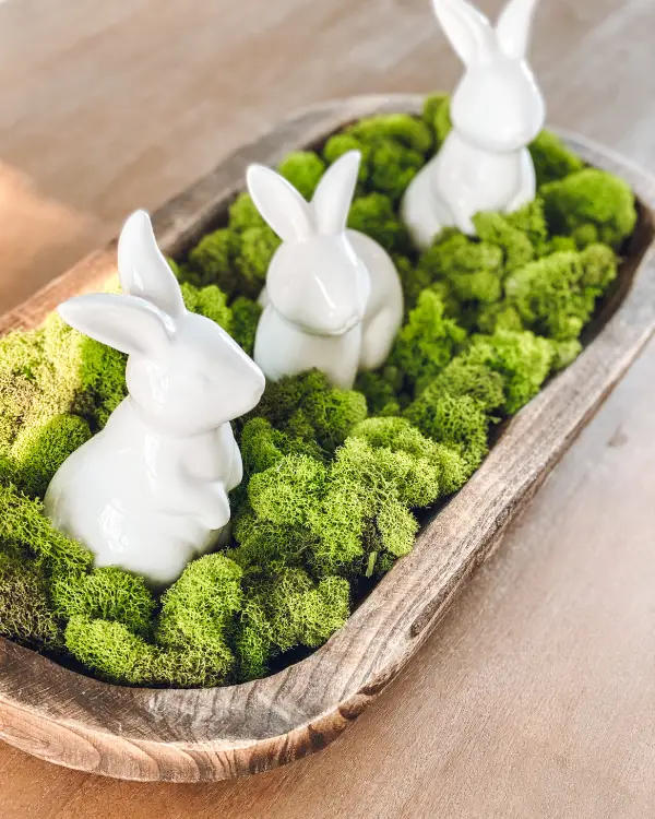 Three white porcelain bunnies sitting in a dough bowl surrounded by green moss.