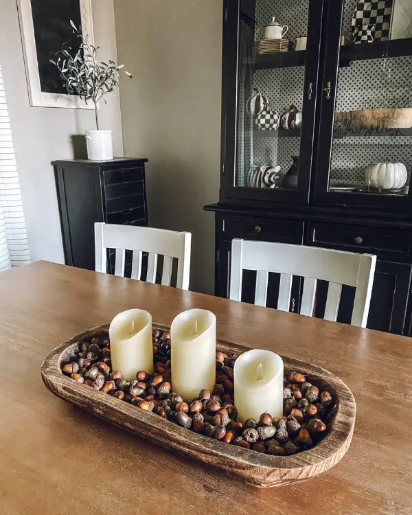 This fall centerpiece idea is white pillar candles in a dough bowl surrounded by acorns.