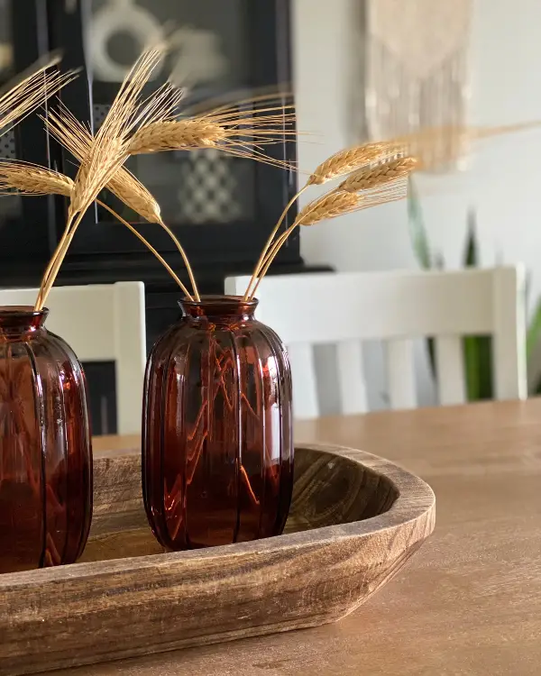 This fall centerpiece idea is a dough bowl with amber vases and wheat stems.