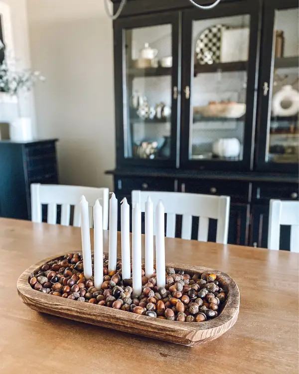 This fall centerpiece idea is white tapered candles in a dough bowl surrounded by acorns.