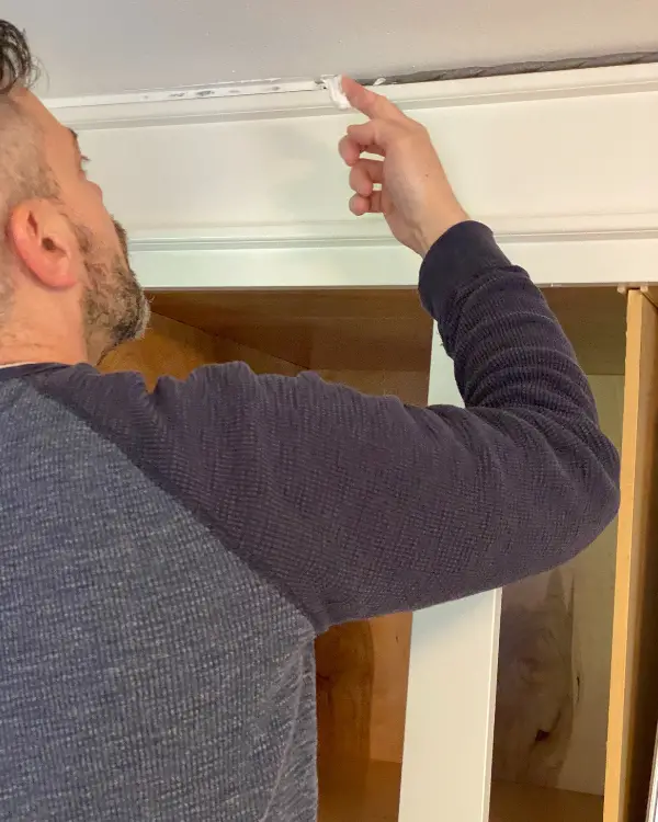 Smoothing the caulk over the backer rod in a larger gap between cabinet and ceiling.