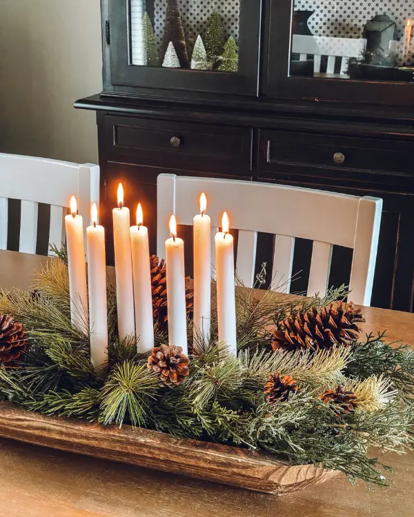 Lit candles and greenery and pine cones in a dough bowl