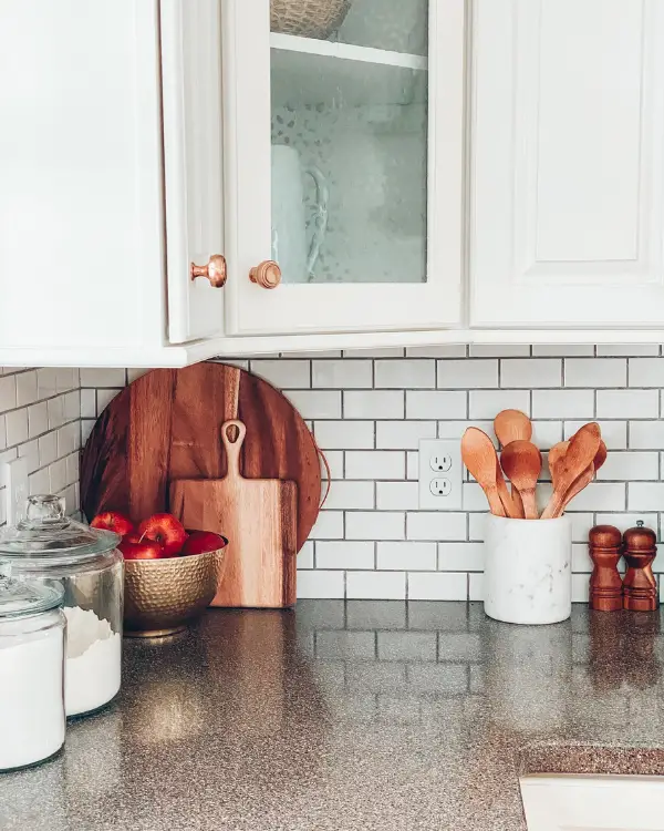 a utensil holder of wooden spoons and a bowl of apples and cutting boards on the kitchen counter