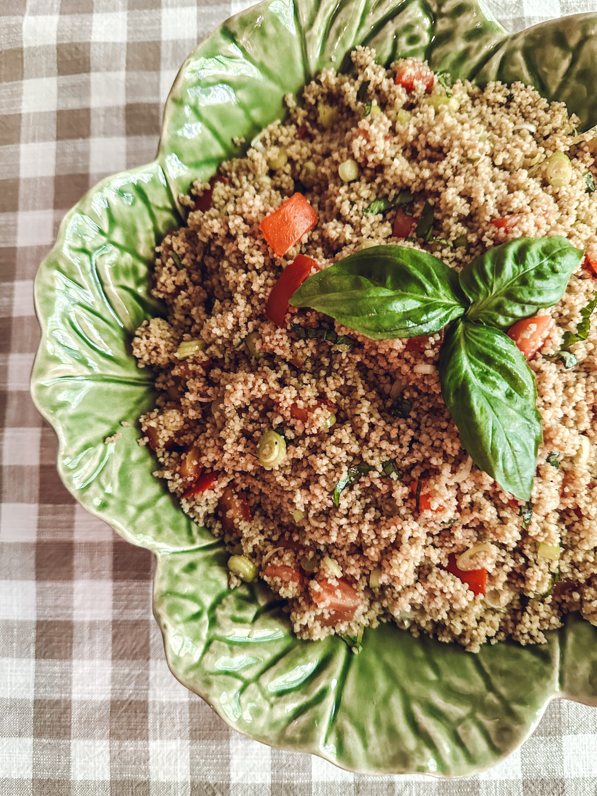 green cabbage leaf bowl containing couscous salad on a brown gingham tablecloth