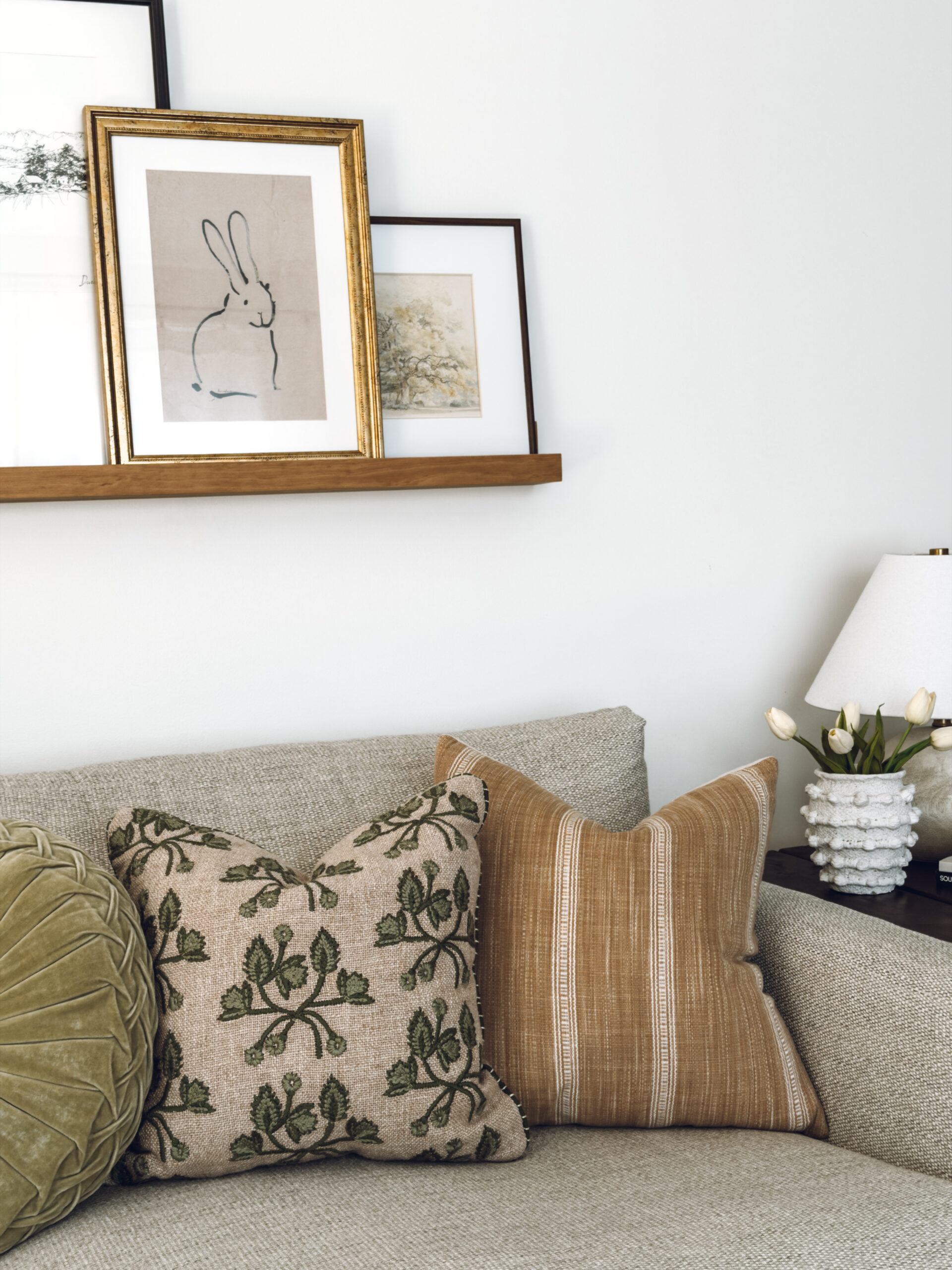 bunny art on the ledge above the couch with a spring pillow with green vines